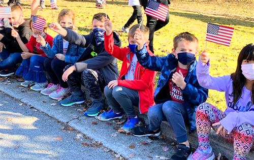 kids sitting on side of parade route waving flags